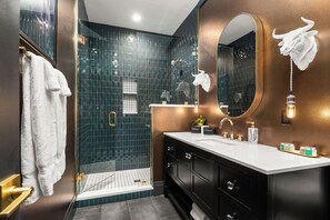 A modern bathroom with a dark tiled shower, a large mirror, and a vanity with a white countertop.