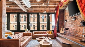 Una sala de estar acogedora con un sofá de cuero, una mesita de centro y una pared de ladrillo con una guitarra.