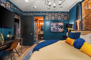 Ein Schlafzimmer mit einem Bett, einem Schreibtisch und einem Stuhl. Eine Tür führt in einen weiteren Raum.