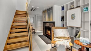 A modern living room with a wooden staircase, a fireplace, a comfortable seating area, and a bookshelf. - LARGE HOME, CLOSE TO THE BEACH! (REHOBOTH BEACH)