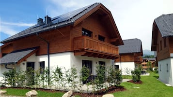 Een modern houten huis met balkon, omgeven door een verzorgde tuin en een grindpad.