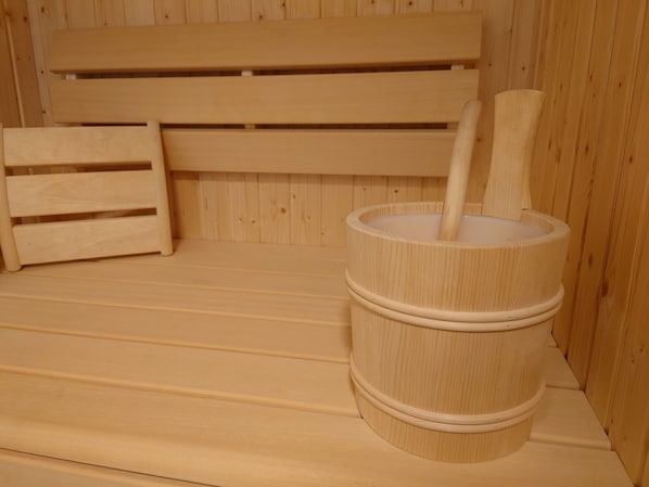 A sauna room with a wooden bench and a wooden bucket with a handle.