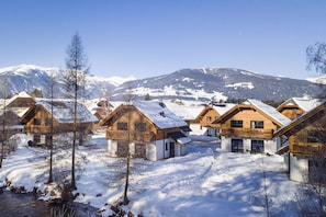 A cluster of wooden chalets with snow-covered roofs, set against a backdrop of snow-capped mountains.