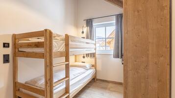 Ein Schlafraum mit Etagenbetten, Holzboden und einem Fenster mit Vorhängen.