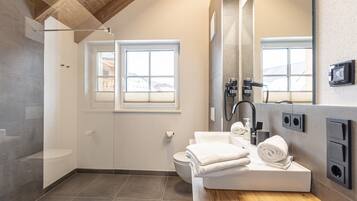 Een moderne badkamer met douche, toilet en wastafel. Er liggen handdoeken op de wastafel en hangt er een grote spiegel boven.