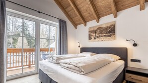 Ein Schlafzimmer mit einem großen Bett, einer Holzbalkendecke, einer Schiebetür zum Balkon und einem Bild an der Wand.