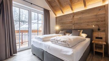 Een slaapkamer met een groot bed, houten balken in het plafond, een nachtkastje en uitzicht op een besneeuwd terras.