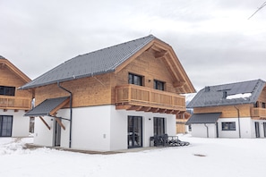 Ett modernt trähus med en balkong, ett garage och en täckt uteplats.