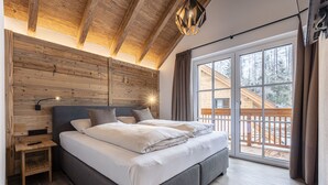Un dormitorio con cabecera de madera, cama con sábanas blancas, mesita de noche con lámpara y vista a una terraza de madera.