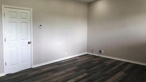 A room with a white door, a ceiling fan, recessed lighting, and a herringbone-patterned wooden floor.