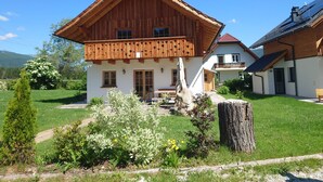 Ein traditionelles Holzhaus mit Balkon, umgeben von einem gepflegten Garten und blauem Himmel.