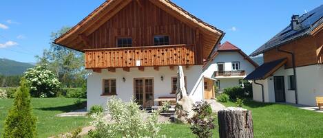 A two-story wooden house with a balcony, surrounded by a well-maintained garden.
