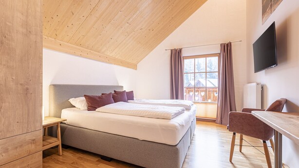 Ein Schlafzimmer mit Holzboden, einem Bett mit Kissen, einem Schreibtisch und einem Fernseher.