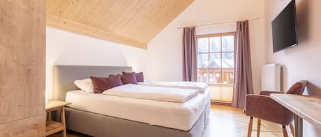 Ein Schlafzimmer mit Holzboden, einem Bett mit Kissen, einem Schreibtisch und einem Fernseher.