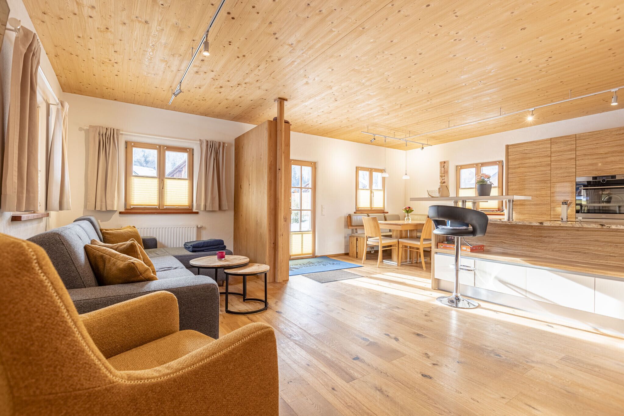 Een ruime woonkamer met een bank, salontafel en een eettafel. In de achtergrond is een keuken zichtbaar met houten kastjes en een aanrecht.