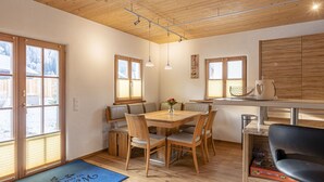 Een eetruimte met een houten tafel en stoelen, een vaas met bloemen en uitzicht op het landschap door grote ramen.