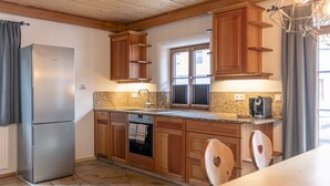 A kitchen with wooden cabinets, a stainless steel refrigerator, a built-in oven, granite countertops, and a window with shutters. - AlpiNest Apartment Samspitze 3 (Mariapfarr)