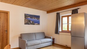 A cozy living room with a grey sofa, wooden flooring, a wooden ceiling, a window with curtains, and a refrigerator. - AlpiNest Apartment Samspitze 3 (Mariapfarr)