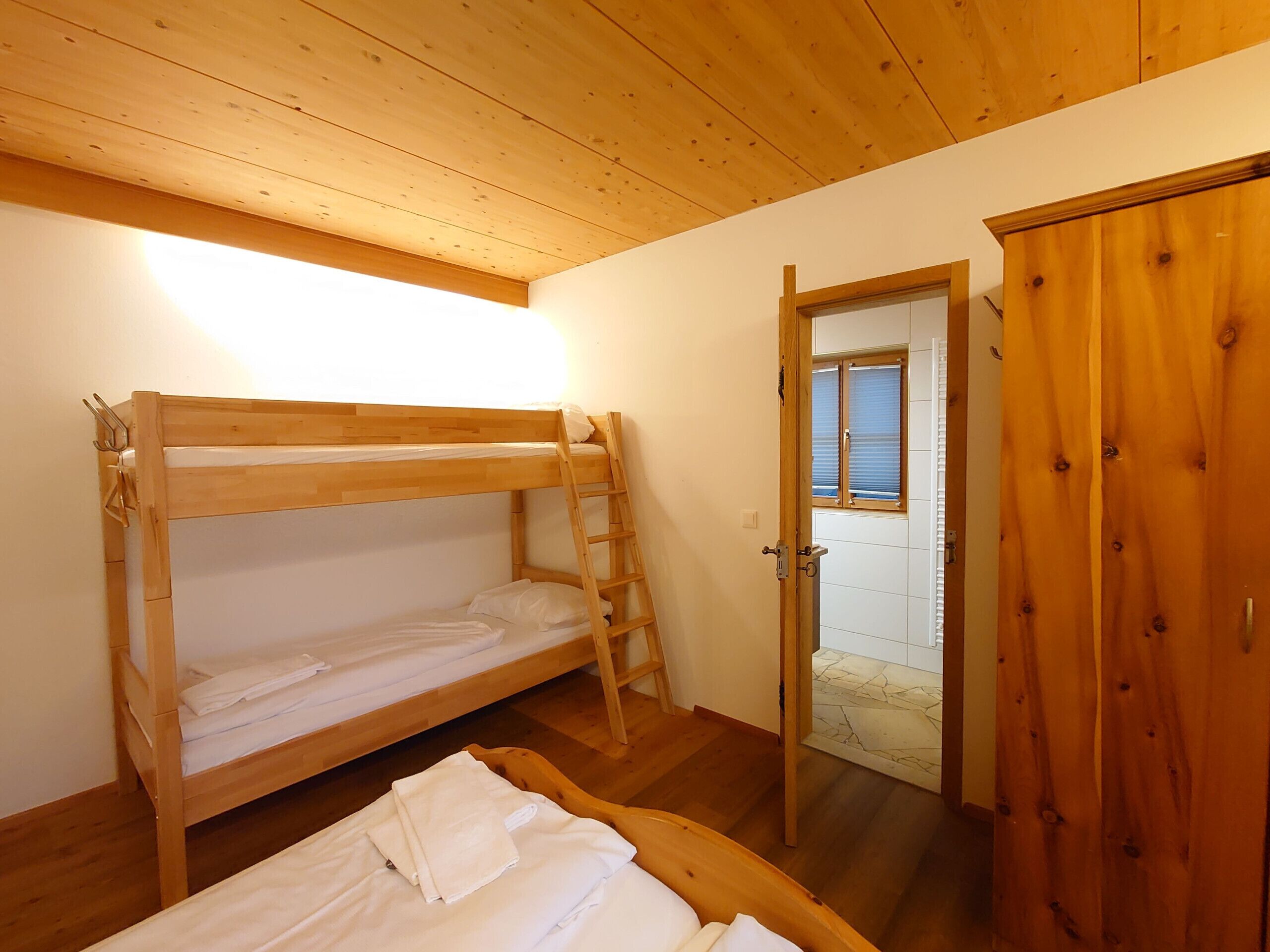 A bunk bed room with a wooden ladder, a wooden door, and a view through a window.