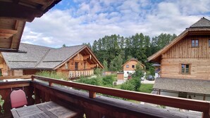 A wooden deck with a table and chairs, overlooking a row of traditional log cabins with sloped roofs and a clear sky. - AlpiNest Apartment Samspitze 2 (Mariapfarr)