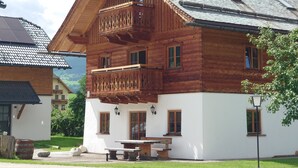 A wooden chalet with a balcony, a table, and a bench outside.