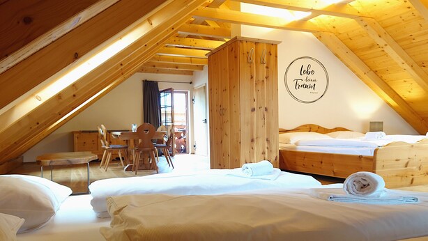A cozy attic bedroom with wooden beams, a dining area, and a bed with neatly made linens.