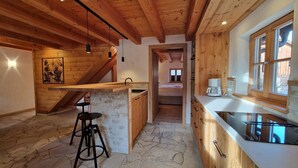 Cocina rústica con suelo de piedra, vigas de madera, una barra y vistas a un dormitorio.