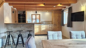 Una cocina moderna con armarios de madera, salpicadero de piedra y un comedor con mesa de madera y taburetes de bar.