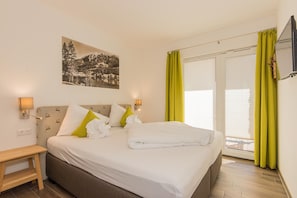 A hotel room with a bed, a nightstand, a wall-mounted lamp, a painting, and a sliding glass door with curtains.
