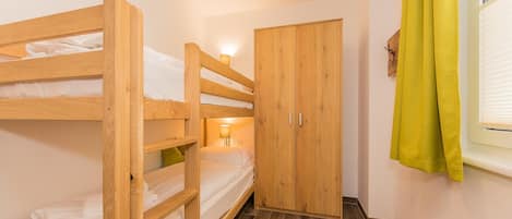 Dormitorio con literas, un armario de madera y una ventana con cortinas.