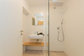 A bathroom with a glass shower enclosure, a sink with a wooden bench, and a mirror above the sink. - Chalet Almrose Zell am See (Zell am See)