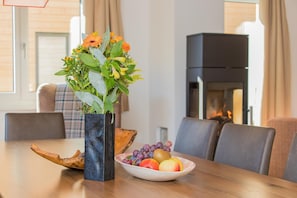 Una mesa de comedor con un florero, un frutero y una chimenea al fondo.