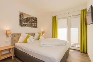 Een hotelkamer met een bed, nachtkastje, een aan de muur bevestigde televisie en een raam met gordijnen.