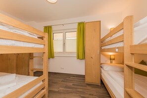 Habitación con literas de madera, una ventana con cortinas, una lámpara de noche y suelo de madera.