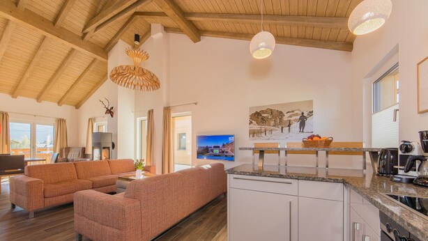 Amplia sala de estar con un conjunto de sofás, una cocina de diseño moderno y un comedor con vistas al exterior.