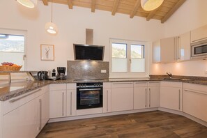 Een moderne keuken met witte kasten, een inbouwoven, een magnetron en een groot raam voor natuurlijk licht.