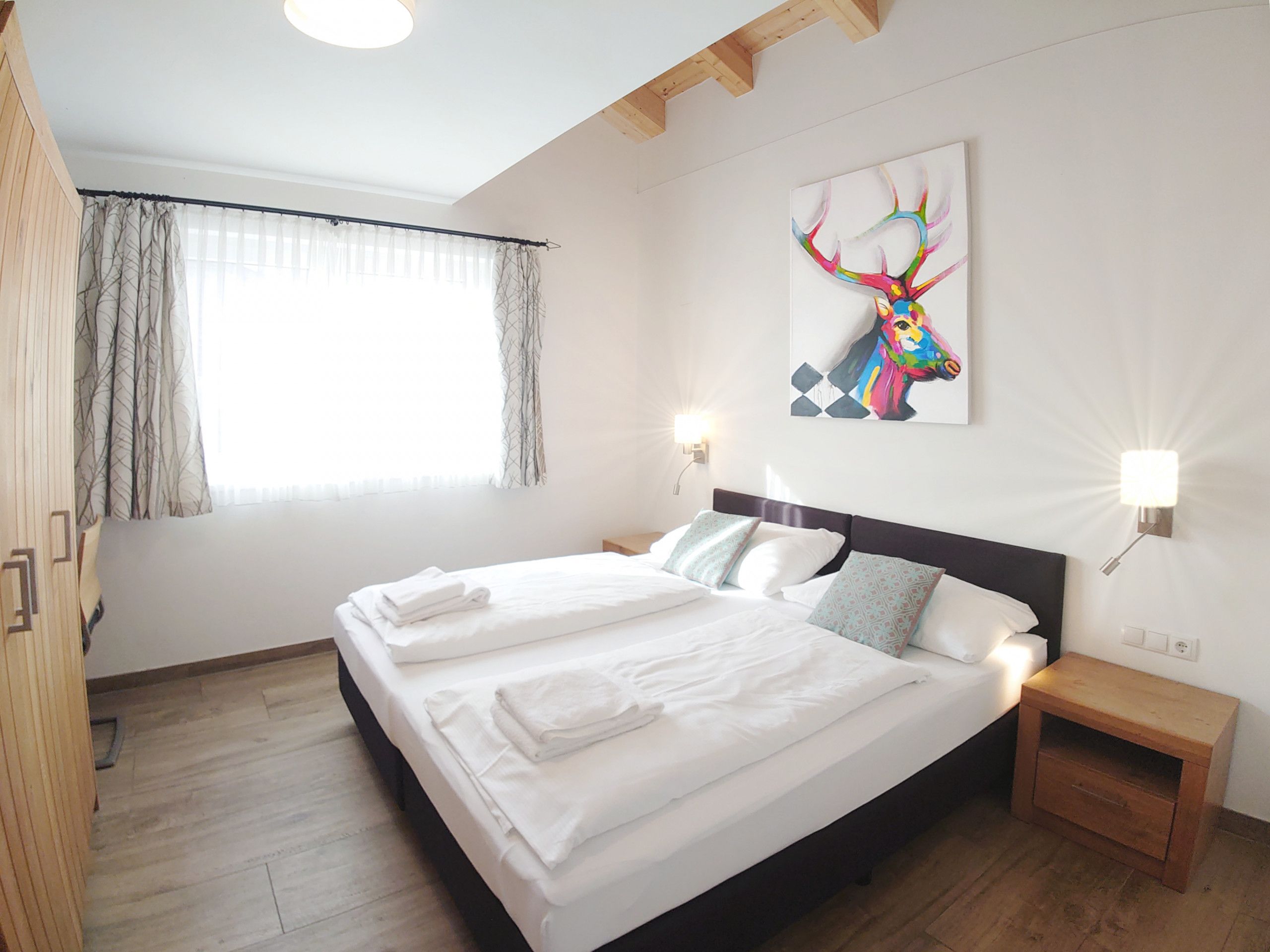 Ein Hotelzimmer mit einem großen Bett, zwei Nachttischen, einem Wandbild und einem Fenster mit Vorhängen.