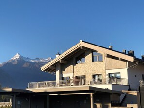 A modern two-story building with a balcony, a mountain view, and a parking area. - Kitzview Terrace Apartment (Zell am See)