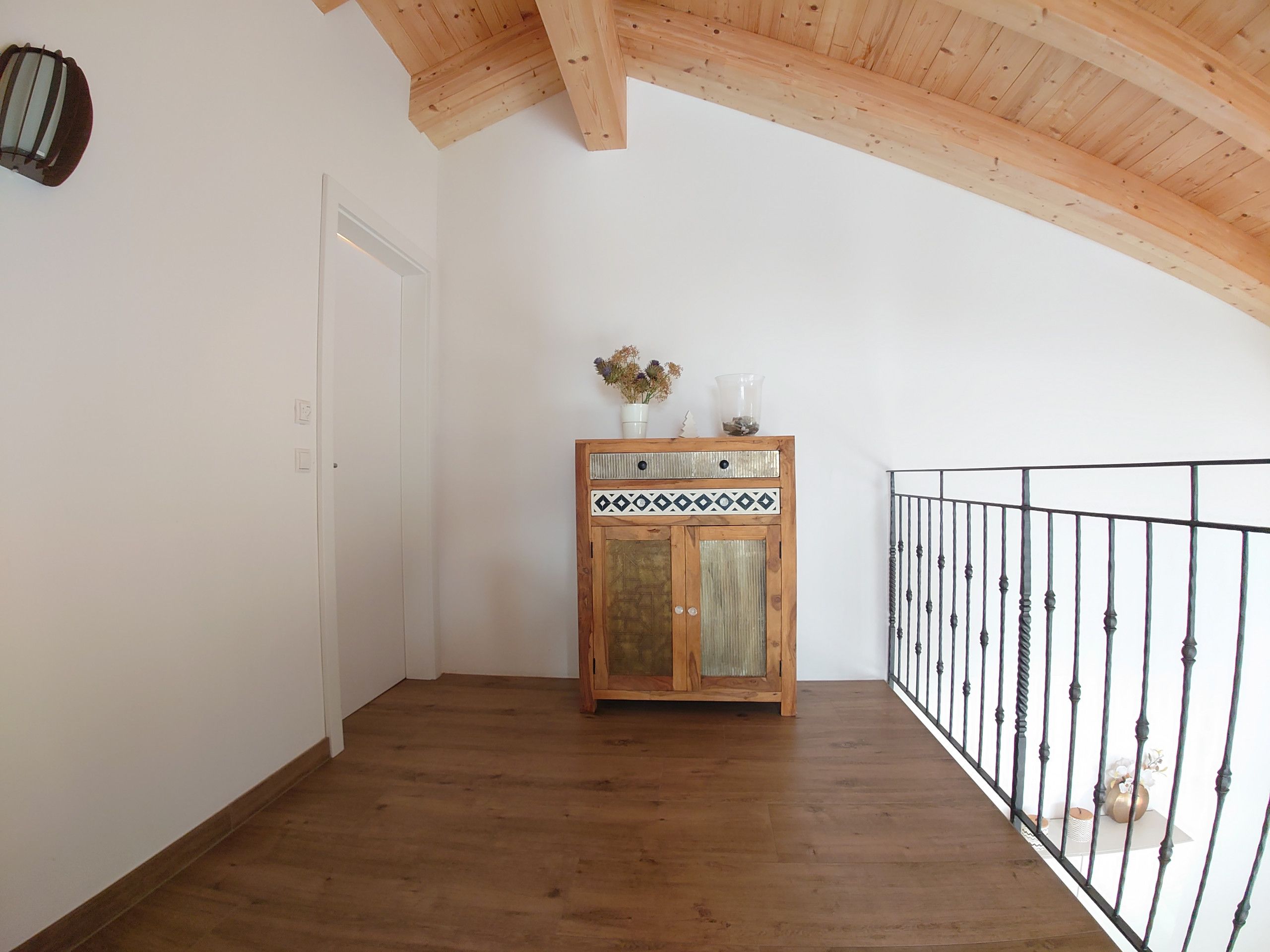 Une pièce avec un plancher en bois, une porte blanche, un meuble en bois orné de carreaux décoratifs et une rambarde en métal.