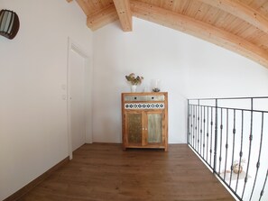 A room with wooden flooring, a wooden cabinet with decorative tiles, a white door, and a black metal railing. - Kitzview Terrace Apartment (Zell am See)
