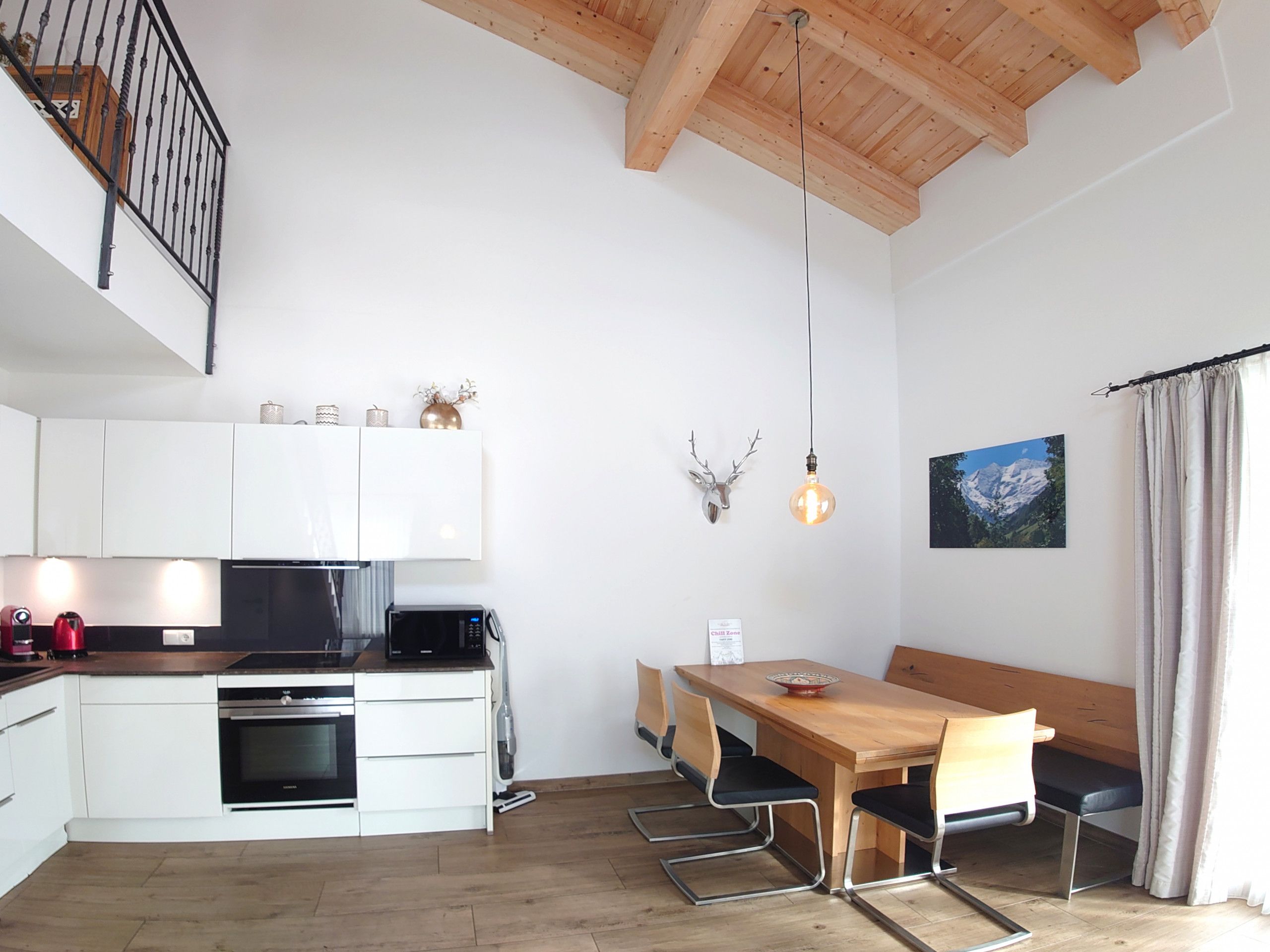 A modern kitchen with white cabinets, a wooden dining table with four chairs, and a hanging light fixture.