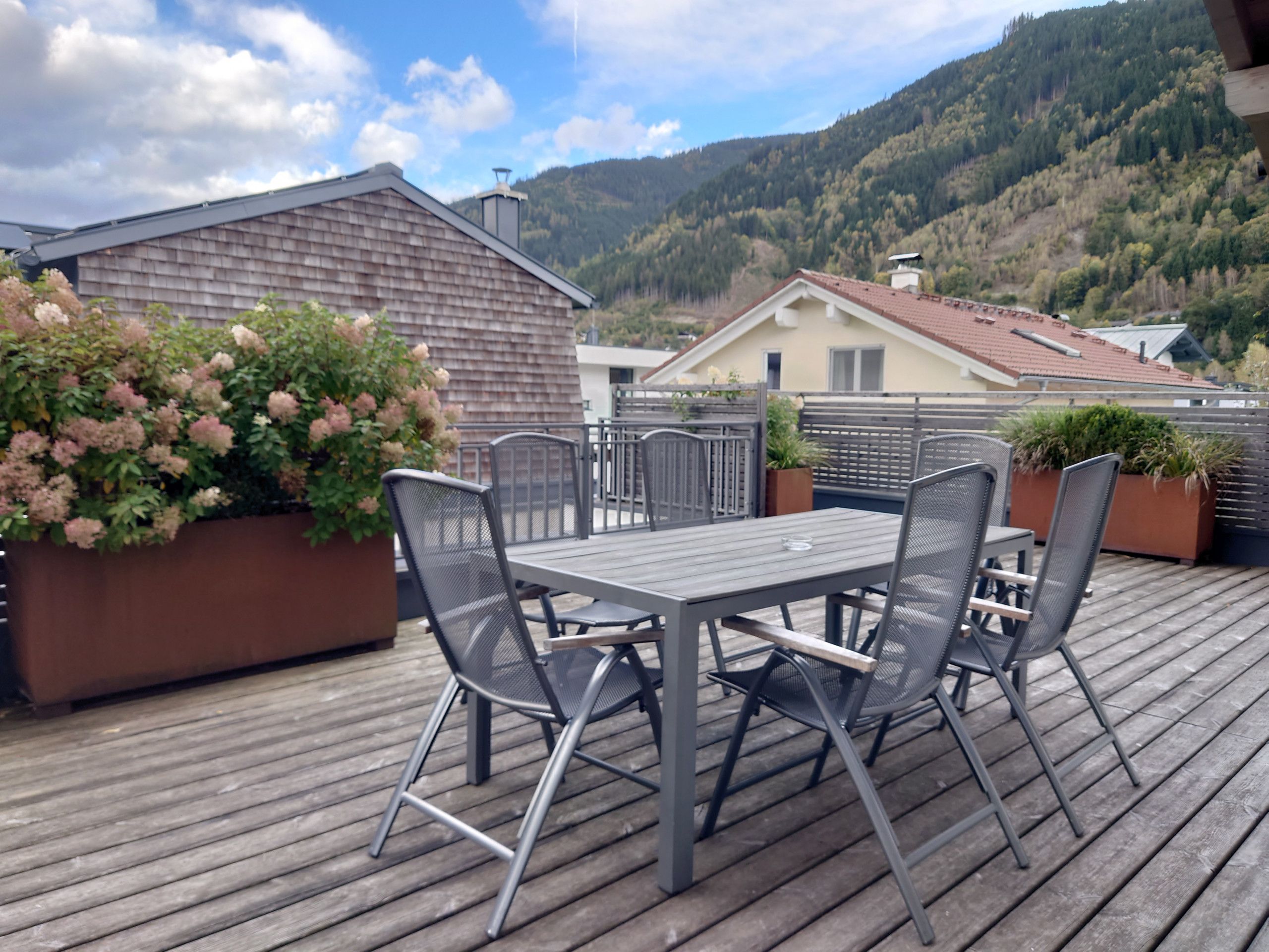 A wooden deck with a table and chairs, surrounded by potted plants and a view of a mountain.