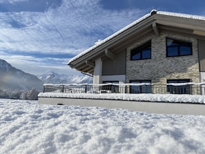 Un edificio moderno con fachada de piedra y amplias ventanas, rodeado de nieve y montañas al fondo.