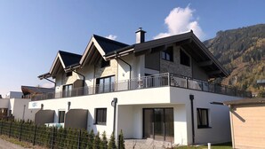 A modern two-story house with a balcony, large windows, and a mountain backdrop. - Kitzview Terrace Apartment (Zell am See)