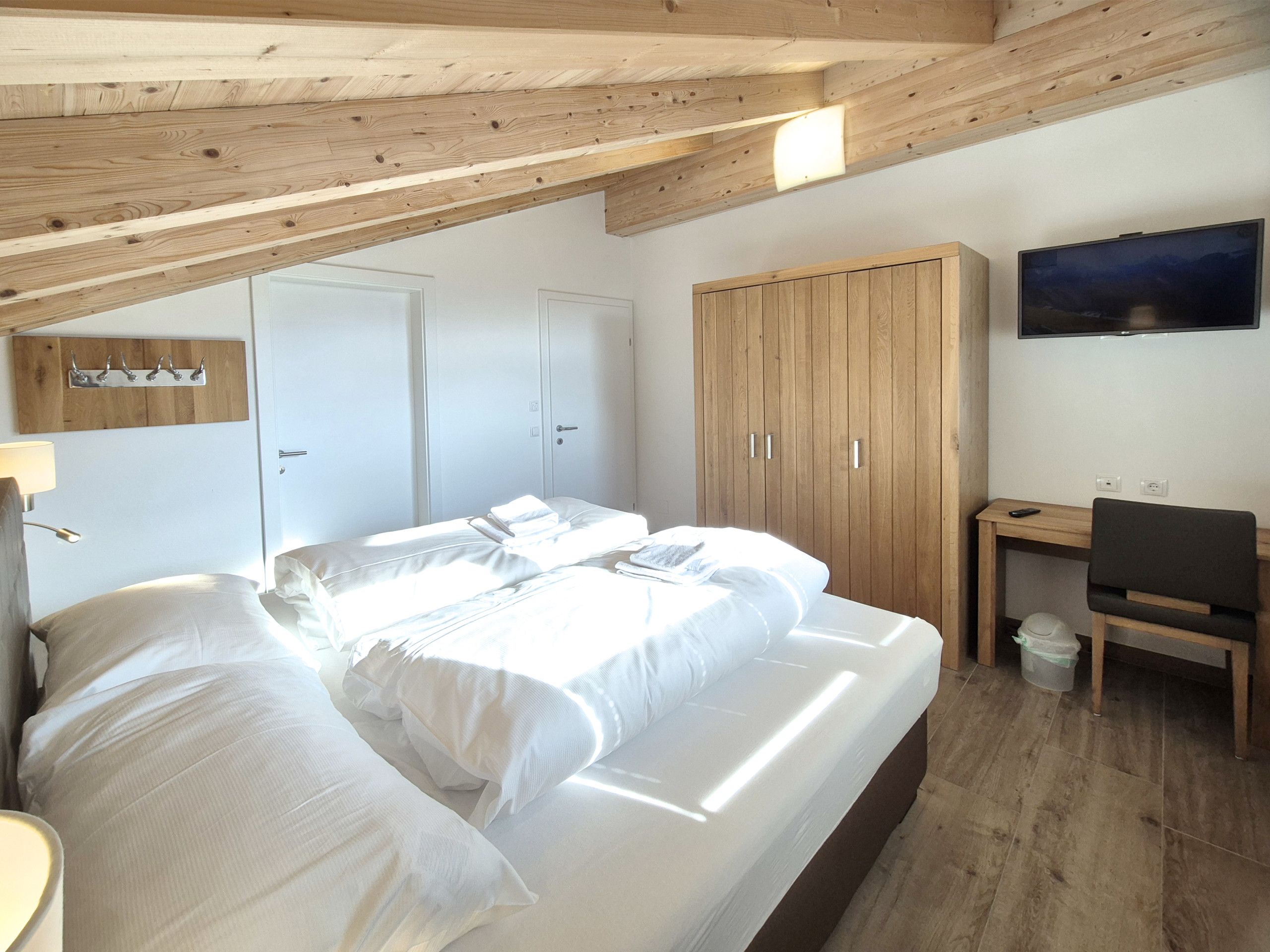 A bedroom with a bed, wooden wardrobe, desk, and a television.