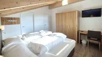 A bedroom with a bed, wooden wardrobe, desk, and a television.