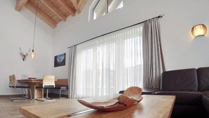A modern living room with a wooden coffee table, a sofa, and a dining area with chairs and a table. - Kitzview Terrace Apartment (Zell am See)