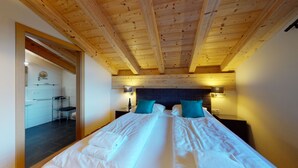 Un dormitorio con una cama grande, dos mesitas de noche con lámparas, techo de madera y vistas a un baño y zona de cocina.
