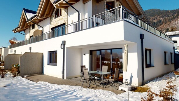 A modern two-story building with a balcony, large windows, and a patio area with outdoor furniture. - Kitzview Idyll Apartment (Zell am See)