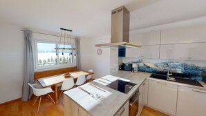 A modern kitchen with a wooden dining table, white chairs, a built-in stove, and a view of a snowy landscape through the window. - Kitzview Idyll Apartment (Zell am See)